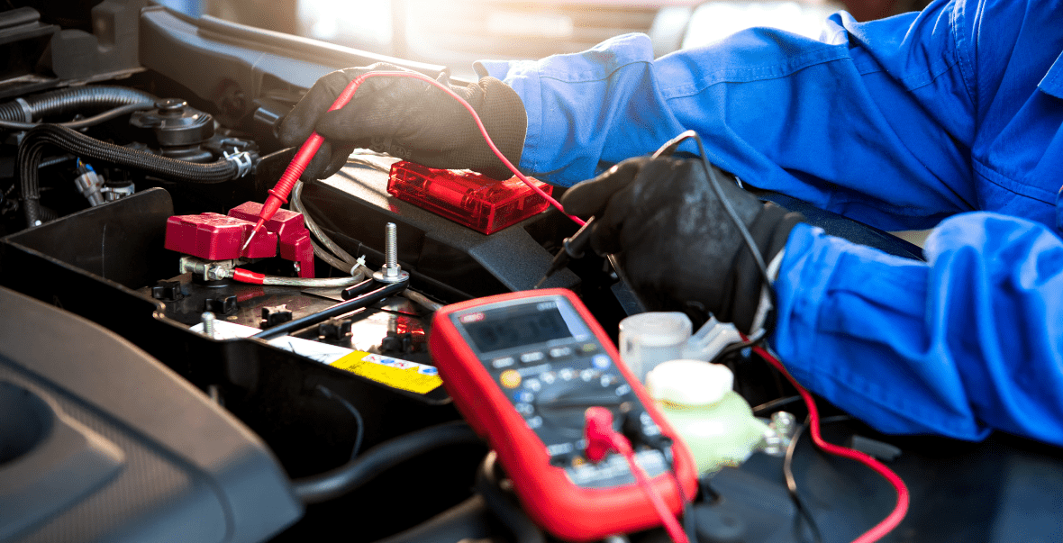Technician using multimeter on car battery