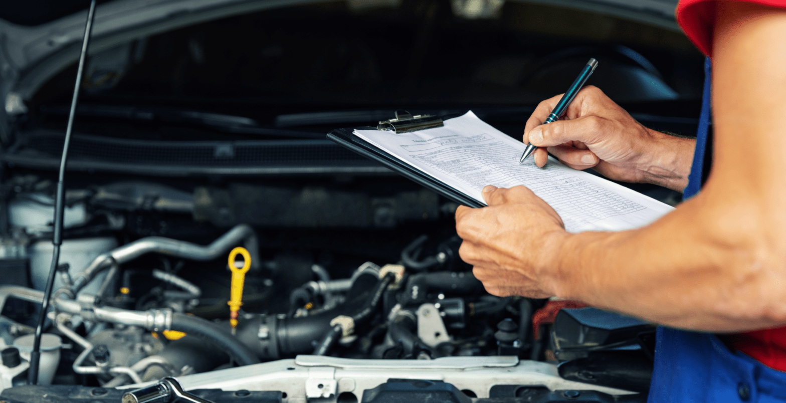 Mechanic inspecting car engine with clipboard